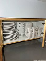 Stacked square dinner and salad plates, bowls and mugs in cupboard