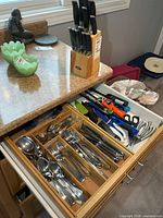 Open drawer showing stainless flatware, utensils and Oster knife block beside