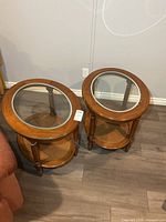 Pair of oval wood end tables with glass tops and cane shelves