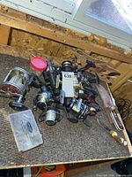 Pile of fishing reels, jar of sinkers, tackle case, fillet knife, pliers on bench