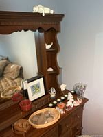 Overview of dresser top with framed art, baskets, belts, candle holder, vases, figurines and shells