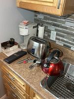 Group shot of Keurig brewer, toaster, kettle, measuring cups and utensils on countertop