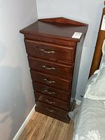 Front view of solid wood 6-drawer chest between wall and bed