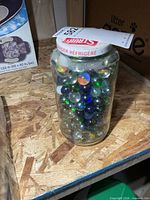 Front view of clear glass jar filled with multicolored marbles, lid visible