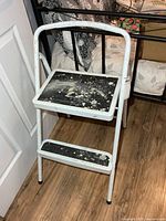 Front view of white metal two-step stool showing paint splatter on black steps