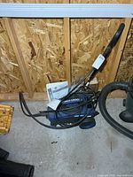 Blue Simoniz pressure washer with handle, hose and manual on floor