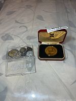 Overview of coin in case and clear box with assorted religious pendants