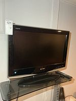 Front view of Sharp Aquos TV on glass shelf with remote