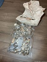 Two clear bags and one crumpled paper bag filled with mixed vintage cutlery on floor