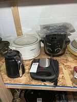Shelf view showing CorningWare slow cooker, Keurig carafe, FineLife grill, Breville fryer with bubble-wrapped plates
