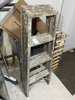 Full view of ladder folded flat showing steps and paint splatter