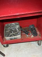 Shelf of red tool chest with metal tin of sockets, pliers and accessories