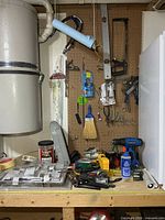 Overall view of pegboard tools, hand broom, saws, pliers, screwdrivers, hardware on bench