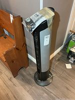 Front view of black and silver tower fan with taped remote bag