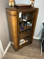 Front angled view of full cabinet showing glass door, shelves, dimensions tag