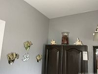 Wall showing three small masks, mirrored bird, two starfish shells on cabinet, glass potpourri jar