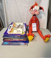 Plush Bill the Cat seated beside stacked books