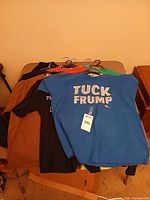 Stack of T-shirts on table, top shirt blue "Tuck Frump"