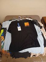 Stack of assorted graphic t-shirts on table, black shirt with Boss graphic on top