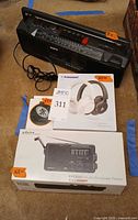 Overall lot showing Sanyo boombox with boxes for Eton FR350 radio, Tronsmart Q20 headphones, and C6 speaker