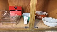 Shelf view showing Pyrex clear glass casseroles, turquoise bowl, Autumn Harvest bowl, white casserole with lid, cheesecake pan box