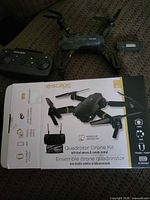 Drone, controller, battery and box on sofa