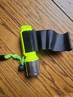 Full view of flashlight showing neon green body, aluminum head, attached Velcro strap, green lanyard