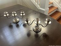 Both silver-plated three-arm candelabras on table