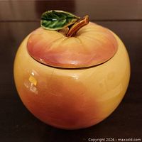 Front view of apple-shaped ceramic cookie jar with lid showing leaf and stem