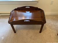 Front angled view of butler's table showing tray sides raised, legs, and finish