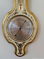 Close-up of barometer dial showing decorative floral border and metal dial