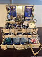 Overall view of jewelry case open with assorted necklaces, bracelets, earrings, brooches, rings and accessories