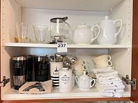 Full cabinet view showing mugs, tumblers, pots, cups, napkins