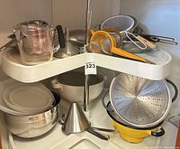 Overall view showing mixing bowls, colanders, strainers, measuring cups and lids on shelf