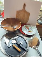 Overall lot showing wood bowl, servers, pizza peel, porcelain plate, red plate, pans, spatulas