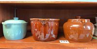 Three vessels on shelf: aqua Denby lidded casserole, brown Denby casserole without lid, brown bean pot with lid