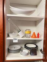 Cabinet view showing stacked white bowls, plates, juicer, funnels, timer and prep tube