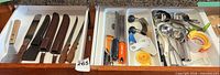 Drawer view of knives with wood handles and assorted stainless/plastic utensils