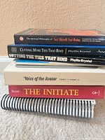 Stack of nine books showing spines including Sai Baba, Phyllis Krystal titles, Voice of the Avatar, The Initiate and spiral-bound volume