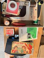 Overview of box with repair kit, threads, Happy Home needle book, tape