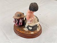 Side view of figurine showing child in washtub, hat on stool, wood base