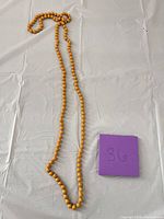 Full view of long mustard yellow bead necklace laid out