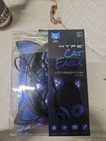 Sealed retail package showing blue/black LED cat ear headphones, brand name and specs visible