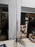 Full view of red spinning rod with attached reel and landing net on table