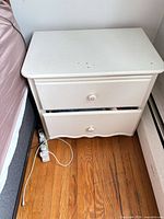 Front angle view of white two-drawer nightstand beside bed