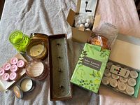 All items grouped: assorted wax candles, flameless tealights set with remote, boxed solar lantern, boxed solar string lights