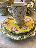Stacked view of mugs, bowls, salad and dinner plates showing floral patterns and molded mug bases