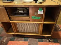 Full front view of console stereo cabinet showing turntable compartment, speaker grille and storage cubbies