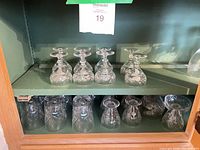 Six stemmed cordials on upper shelf, four tumblers on lower shelf of cabinet