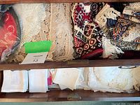 Drawer view showing grouped lace doilies, folded napkins, and patterned woven pieces